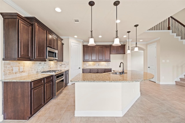 kitchen featuring a center island with sink, sink, hanging light fixtures, light stone counters, and stainless steel appliances