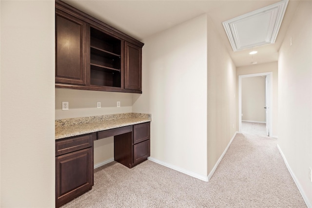 kitchen featuring light stone counters, dark brown cabinetry, built in desk, and light carpet