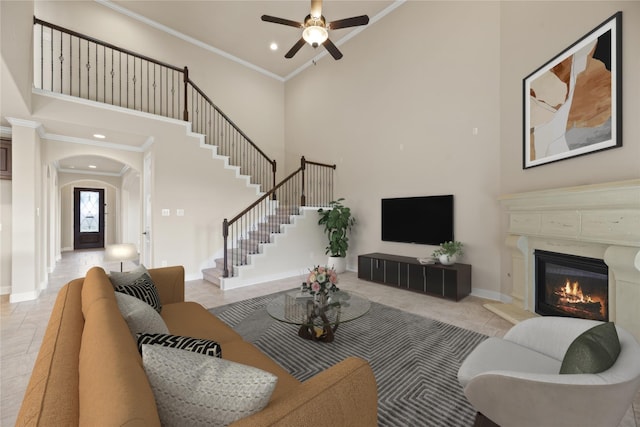 living room with crown molding, a fireplace, ceiling fan, and a high ceiling