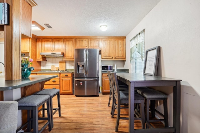 kitchen with appliances with stainless steel finishes, light wood-type flooring, a textured ceiling, and a kitchen breakfast bar