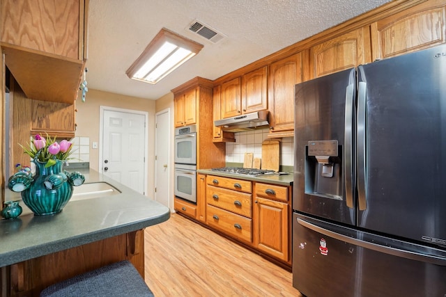 kitchen featuring tasteful backsplash, stainless steel appliances, a textured ceiling, and light hardwood / wood-style floors