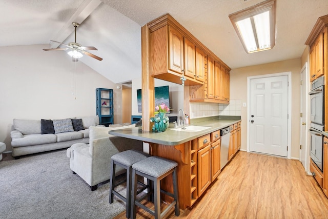 kitchen featuring lofted ceiling with beams, sink, light hardwood / wood-style flooring, stainless steel dishwasher, and a breakfast bar area