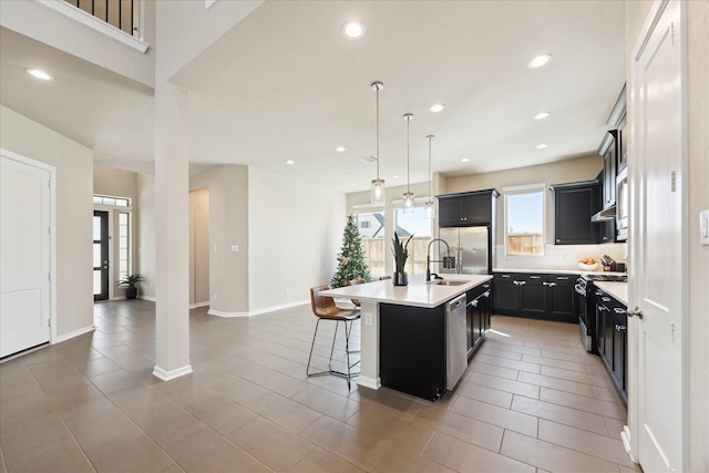 kitchen featuring a kitchen bar, stainless steel appliances, decorative light fixtures, tile patterned flooring, and an island with sink