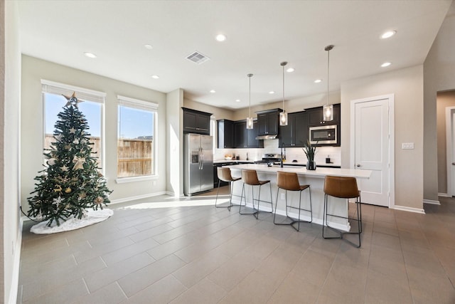 kitchen featuring a kitchen island with sink, hanging light fixtures, decorative backsplash, appliances with stainless steel finishes, and a kitchen bar