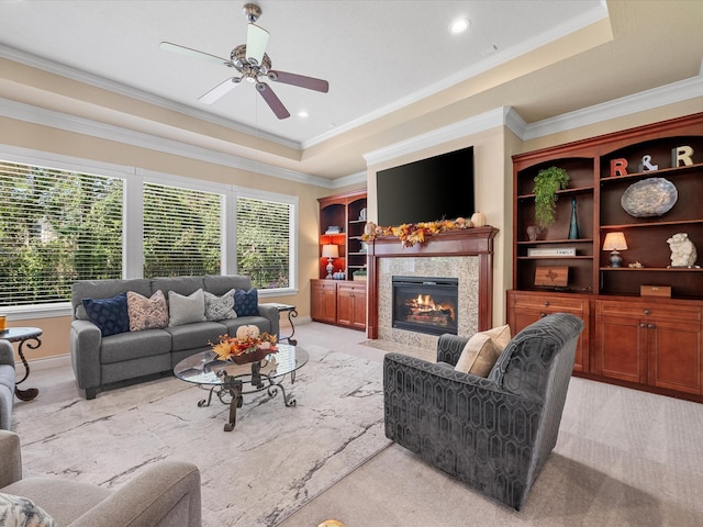 living room featuring a raised ceiling, light carpet, a high end fireplace, and ornamental molding