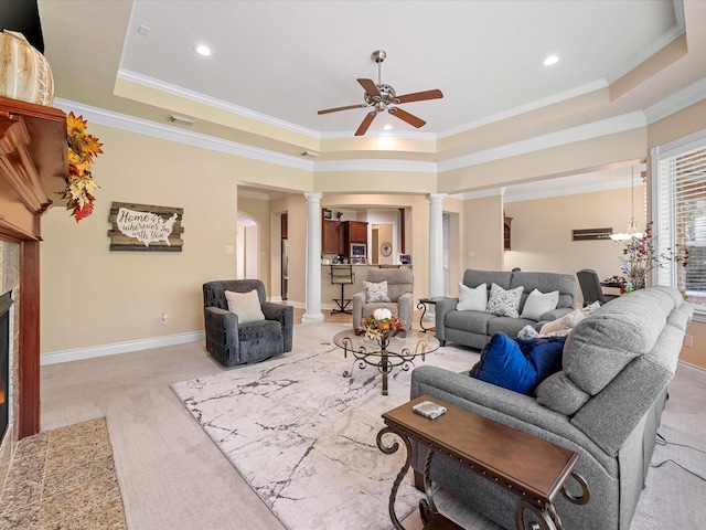 carpeted living room featuring a tray ceiling, decorative columns, ornamental molding, and ceiling fan