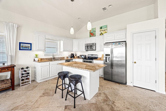 kitchen with light stone countertops, appliances with stainless steel finishes, sink, white cabinets, and a kitchen island