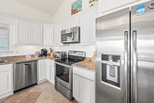 kitchen featuring appliances with stainless steel finishes, vaulted ceiling, white cabinetry, and dark stone countertops