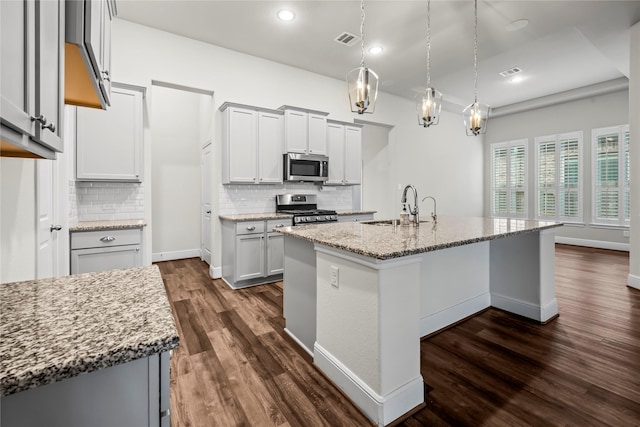 kitchen with dark hardwood / wood-style floors, sink, stainless steel appliances, and an island with sink