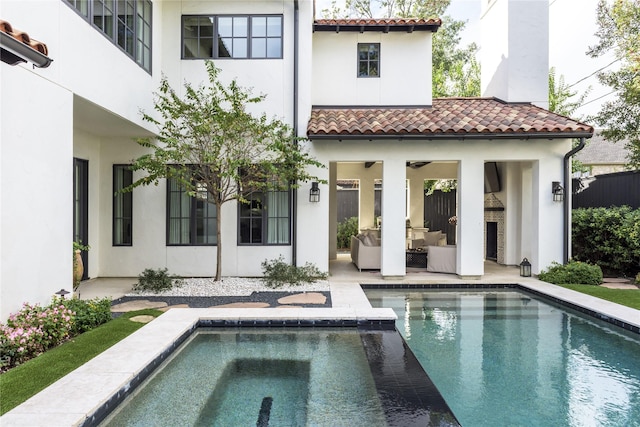 back of property with an outdoor living space with a fireplace, ceiling fan, a swimming pool with hot tub, and a patio