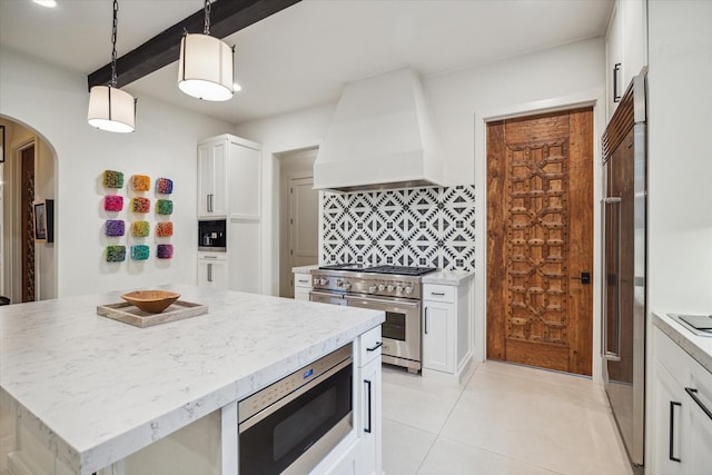 kitchen featuring tasteful backsplash, built in appliances, pendant lighting, white cabinets, and custom range hood