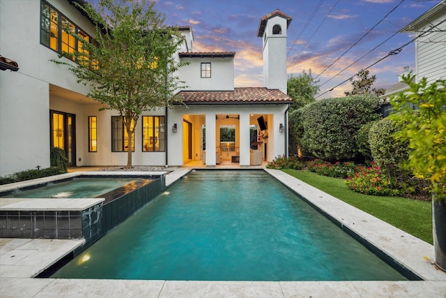 pool at dusk featuring ceiling fan, a patio area, and an in ground hot tub