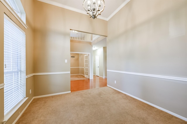 carpeted spare room featuring a high ceiling, an inviting chandelier, and crown molding