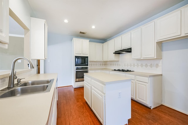 kitchen featuring black microwave, stainless steel oven, sink, decorative backsplash, and hardwood / wood-style flooring