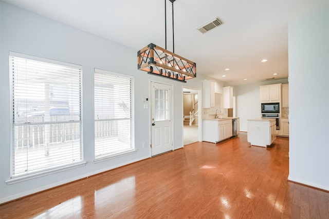 kitchen with appliances with stainless steel finishes, sink, pendant lighting, a center island, and light hardwood / wood-style floors