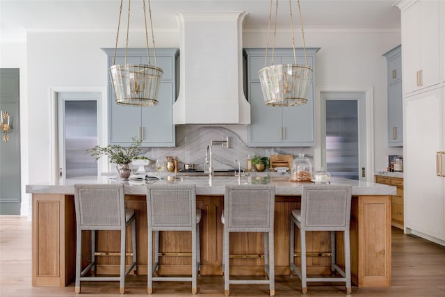 kitchen with light hardwood / wood-style flooring, backsplash, crown molding, gray cabinets, and a breakfast bar