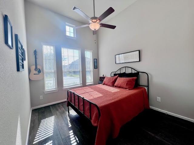 bedroom with ceiling fan, dark hardwood / wood-style flooring, and a towering ceiling