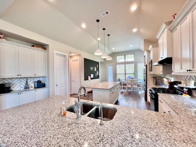 kitchen featuring stainless steel range, sink, dark hardwood / wood-style flooring, an island with sink, and decorative light fixtures