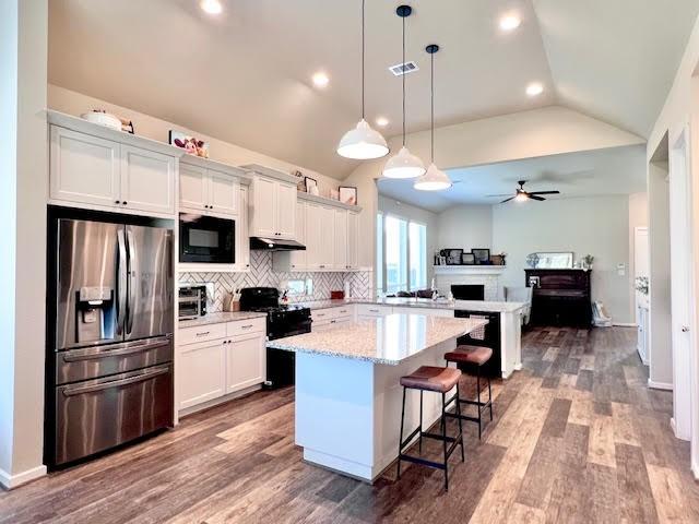 kitchen with a breakfast bar, black appliances, white cabinets, a kitchen island, and lofted ceiling