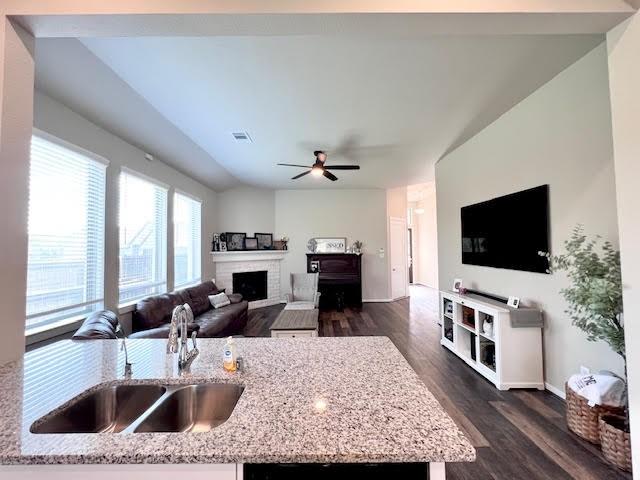 kitchen with light stone countertops, dark hardwood / wood-style flooring, a brick fireplace, and sink