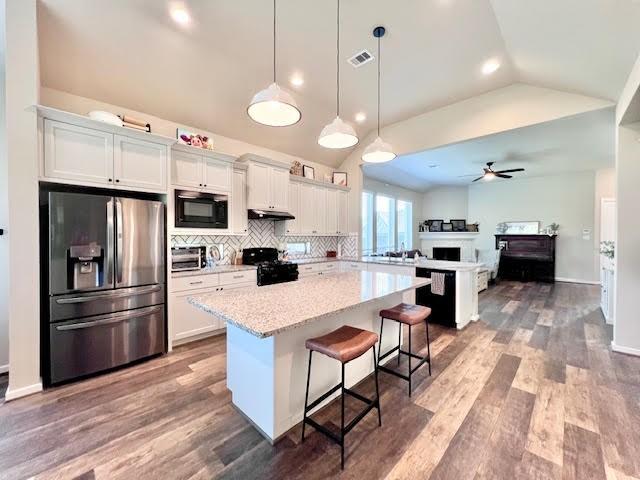 kitchen with a kitchen bar, a center island, white cabinets, and black appliances