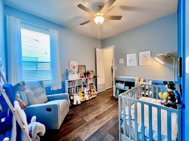 bedroom with ceiling fan, dark hardwood / wood-style floors, and a crib