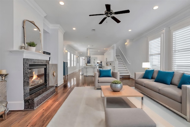 living room featuring hardwood / wood-style floors, ceiling fan, ornamental molding, and a fireplace