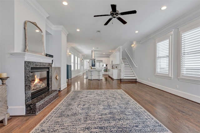 living room with ceiling fan, a high end fireplace, dark hardwood / wood-style floors, and ornamental molding