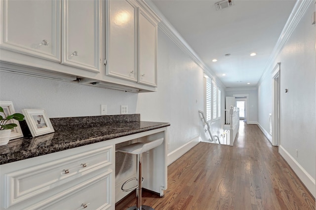 kitchen featuring white cabinets, dark stone counters, light hardwood / wood-style floors, and ornamental molding