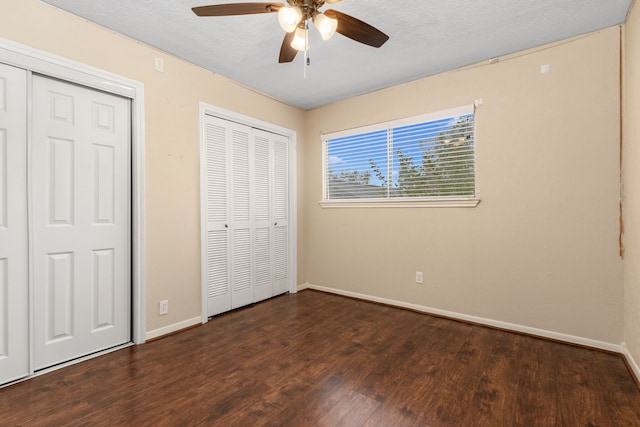 unfurnished bedroom with ceiling fan, dark hardwood / wood-style floors, a textured ceiling, and multiple closets