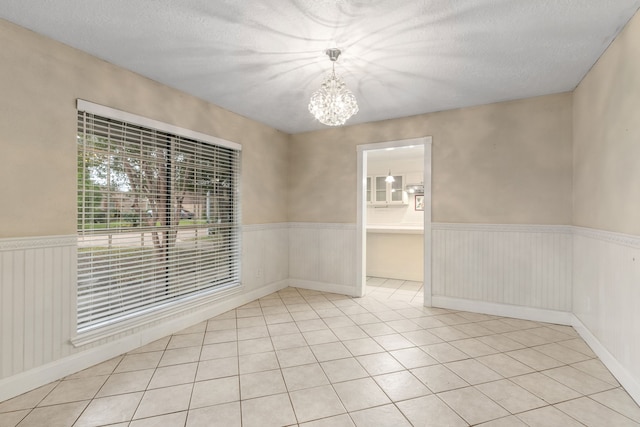 empty room featuring light tile patterned floors, a textured ceiling, and a notable chandelier