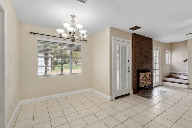 empty room with ceiling fan with notable chandelier, light tile patterned flooring, a textured ceiling, and a brick fireplace