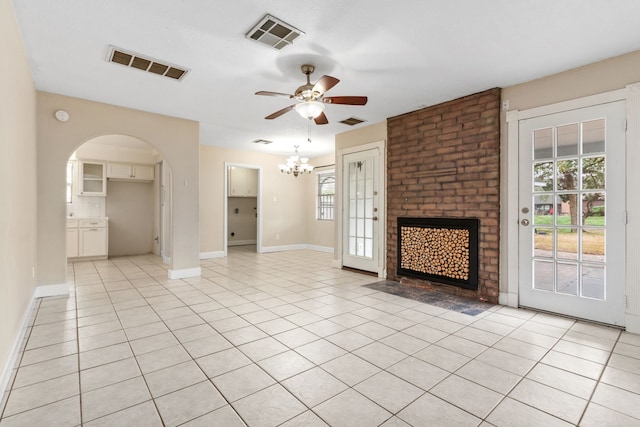 unfurnished living room with light tile patterned floors, ceiling fan with notable chandelier, and a brick fireplace