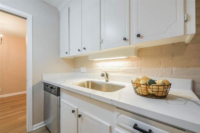 kitchen with light stone countertops, light wood-type flooring, stainless steel dishwasher, white cabinetry, and a sink