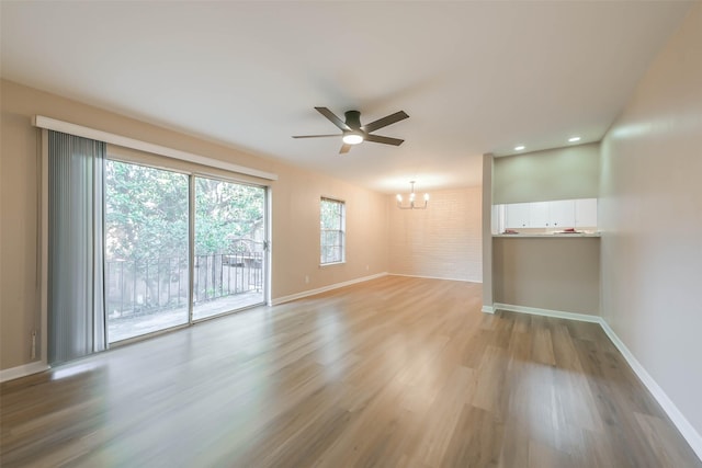 empty room with ceiling fan with notable chandelier and light hardwood / wood-style floors