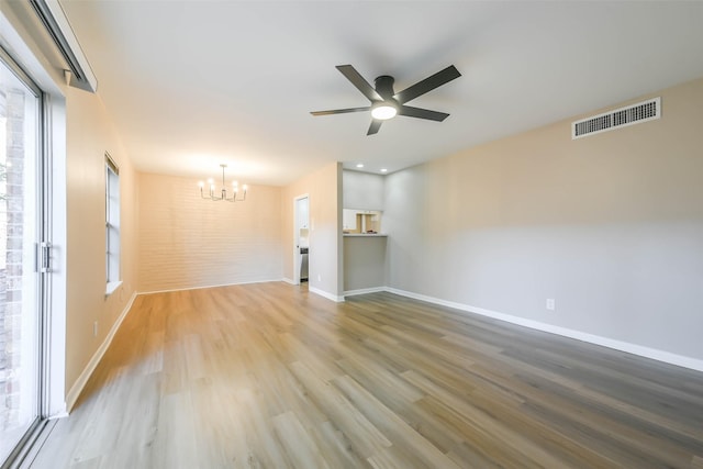 unfurnished room with ceiling fan with notable chandelier, light wood-type flooring, visible vents, and baseboards