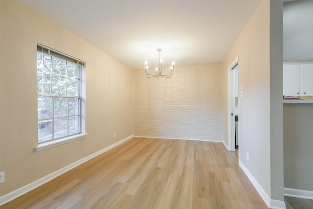 unfurnished dining area featuring light wood-type flooring, brick wall, baseboards, and a chandelier