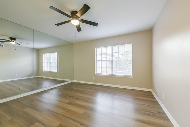 empty room featuring a ceiling fan, visible vents, baseboards, and wood finished floors