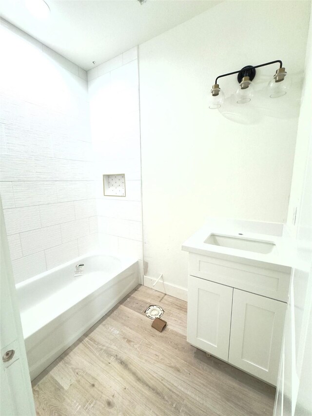 bathroom with hardwood / wood-style flooring, tiled shower / bath, and vanity