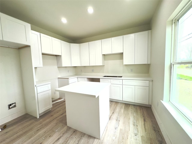 kitchen with white cabinetry, a center island, black electric cooktop, and light hardwood / wood-style flooring