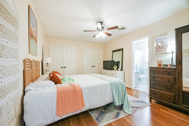 bedroom featuring light wood-type flooring, ceiling fan, two closets, and connected bathroom