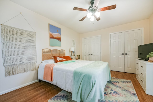 bedroom with baseboards, wood finished floors, multiple closets, and ceiling fan