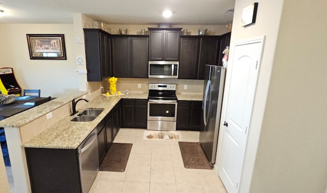 kitchen featuring kitchen peninsula, stainless steel appliances, light stone countertops, and sink