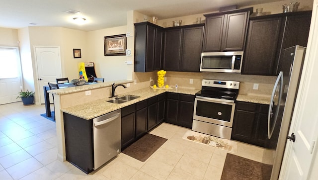 kitchen featuring kitchen peninsula, appliances with stainless steel finishes, light stone counters, sink, and light tile patterned floors