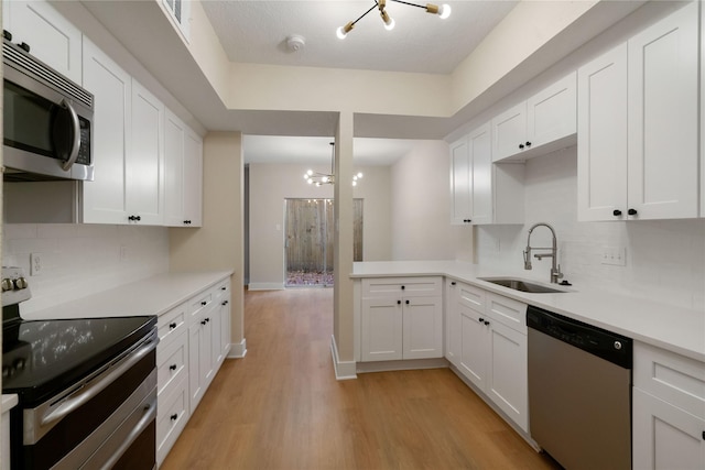 kitchen with stainless steel appliances, white cabinetry, a notable chandelier, and sink