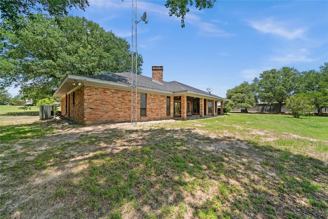 rear view of house with central air condition unit and a yard