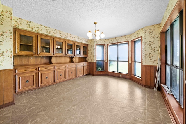 unfurnished dining area featuring wooden walls, a textured ceiling, and a notable chandelier