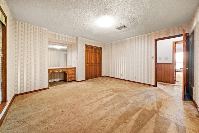 unfurnished bedroom featuring built in desk, a textured ceiling, light carpet, and a closet