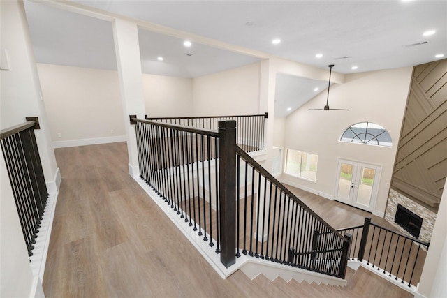 staircase with ceiling fan, a fireplace, a towering ceiling, and hardwood / wood-style floors