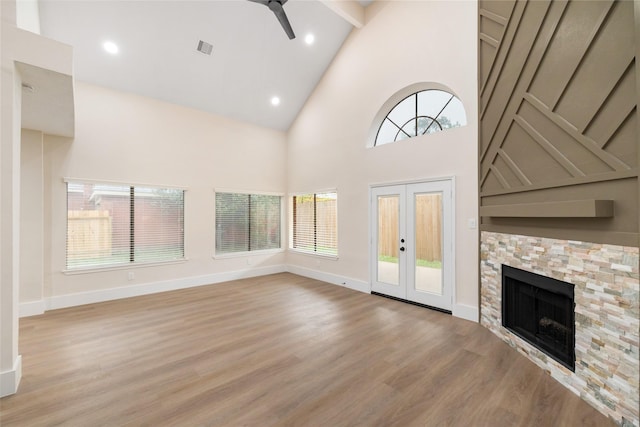 unfurnished living room featuring high vaulted ceiling, french doors, a stone fireplace, light hardwood / wood-style flooring, and ceiling fan